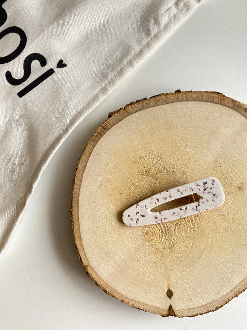 Barrette triangulaire blanche et éclats roses posé sur un rondin en bois